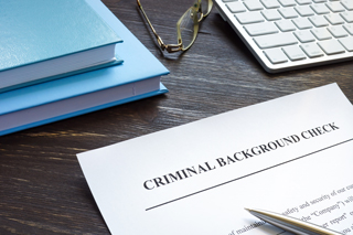 Paper with criminal background check as the title, books and a pair of glasses in the background